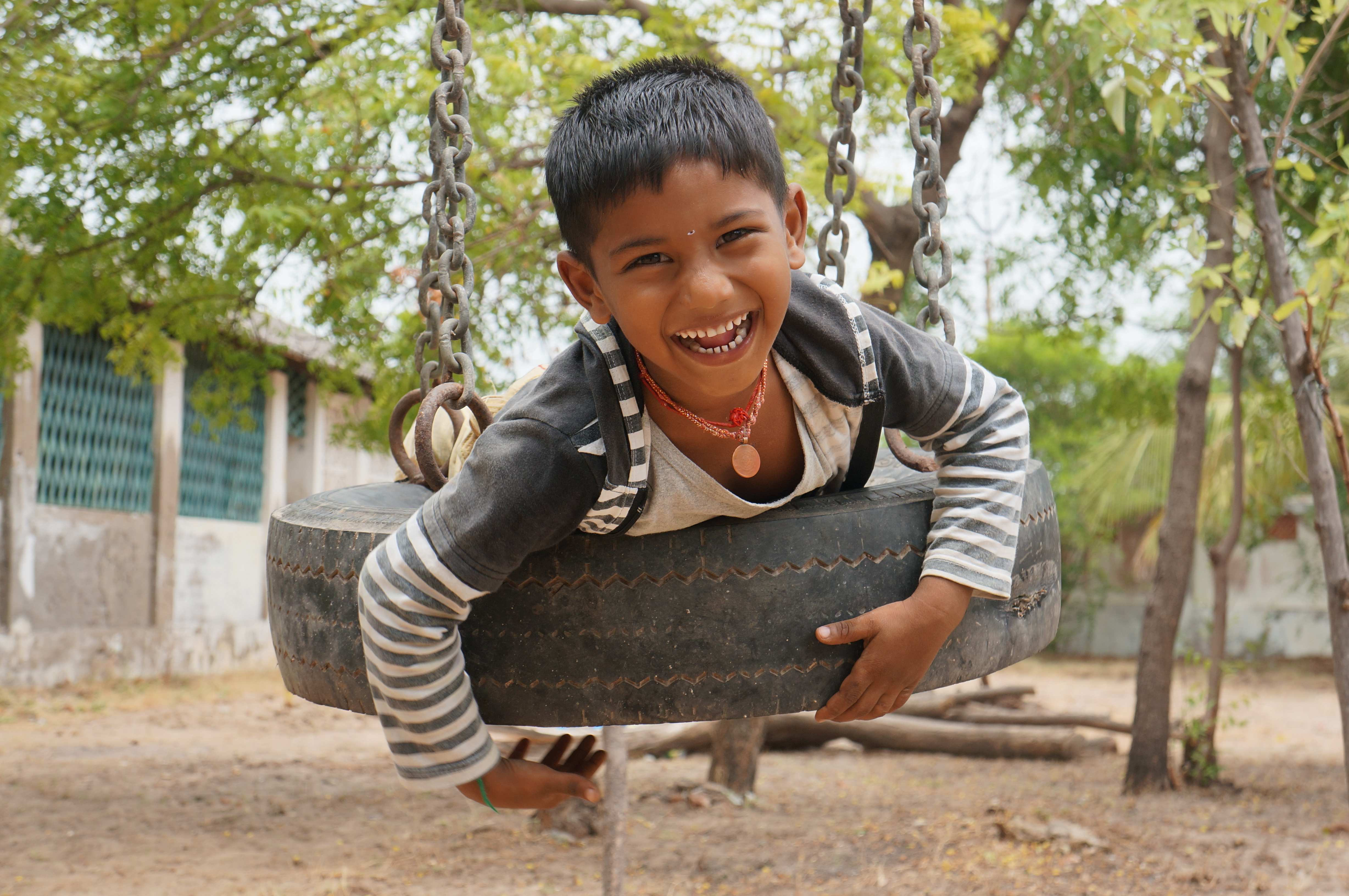 Lachender Bub auf Reifenschaukel, Südindien 