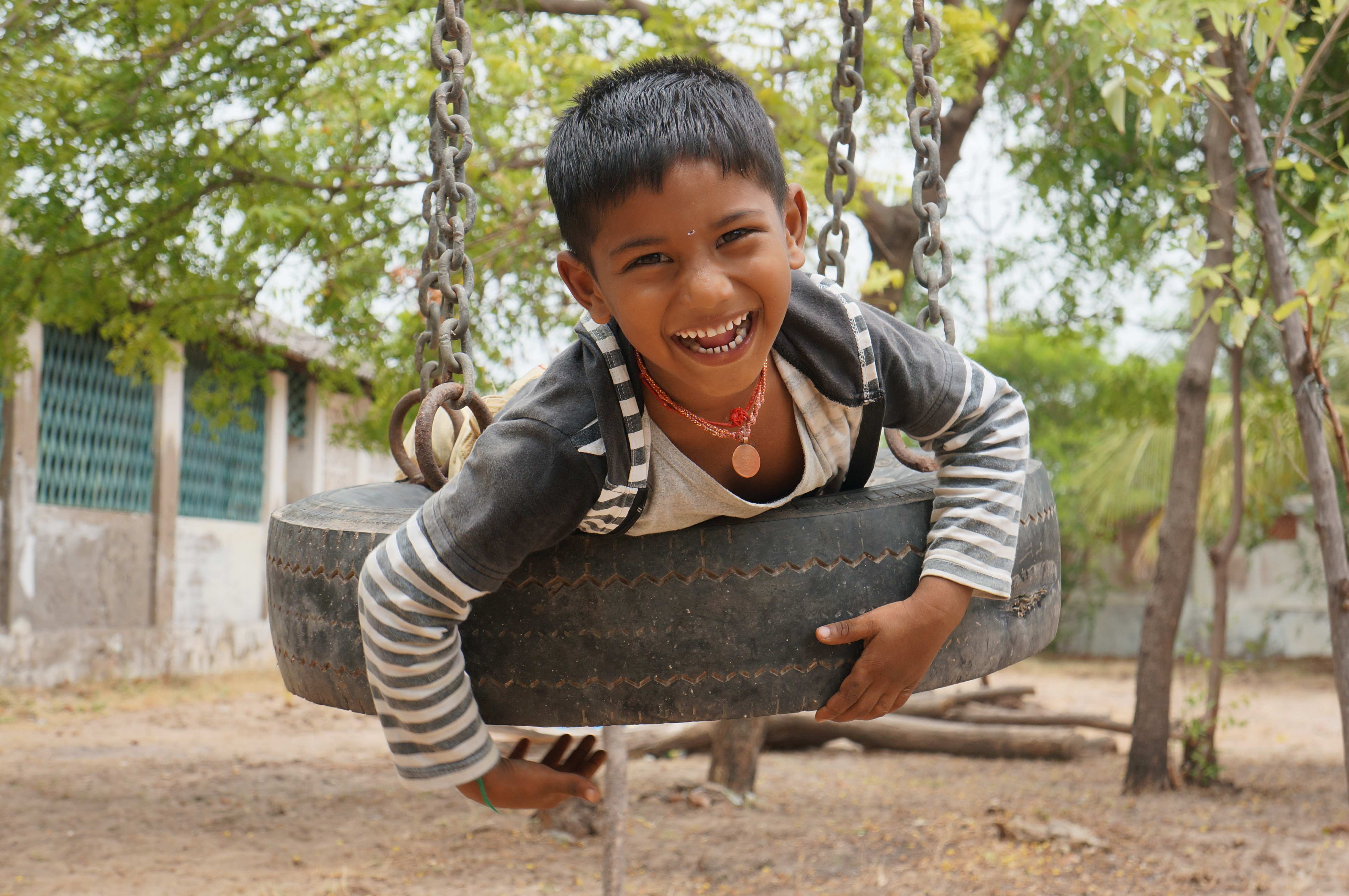 Lachender Bub auf Reifenschaukel, Südindien Lachender Bub auf Reifenschaukel, Südindien