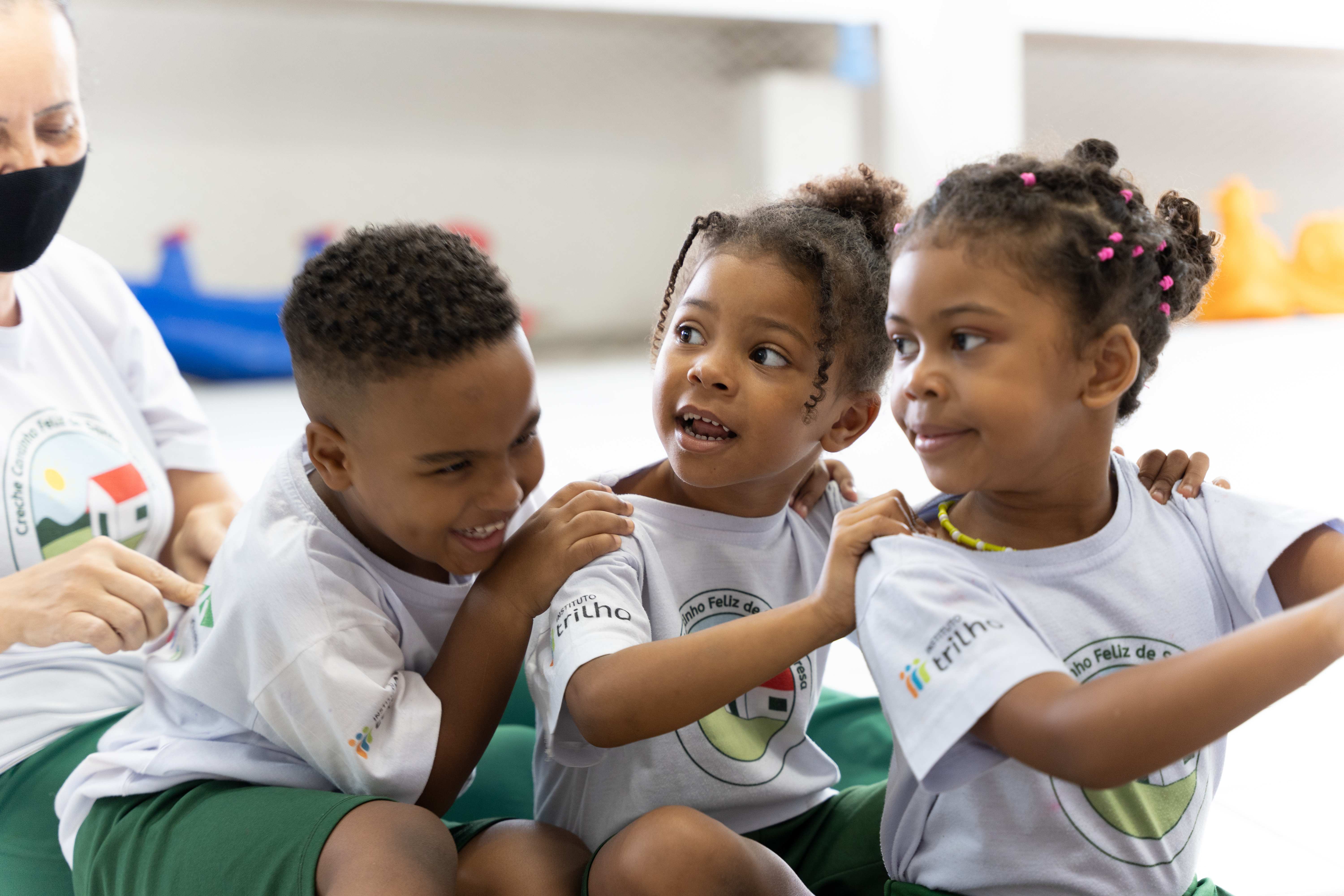 Drei Kinder sitzen lachend hintereinander und fassen sich an den Schultern. (Quelle: Christian Nusch) Drei Kinder sitzen lachend hintereinander und fassen sich an den Schultern. (Quelle: Christian Nusch)