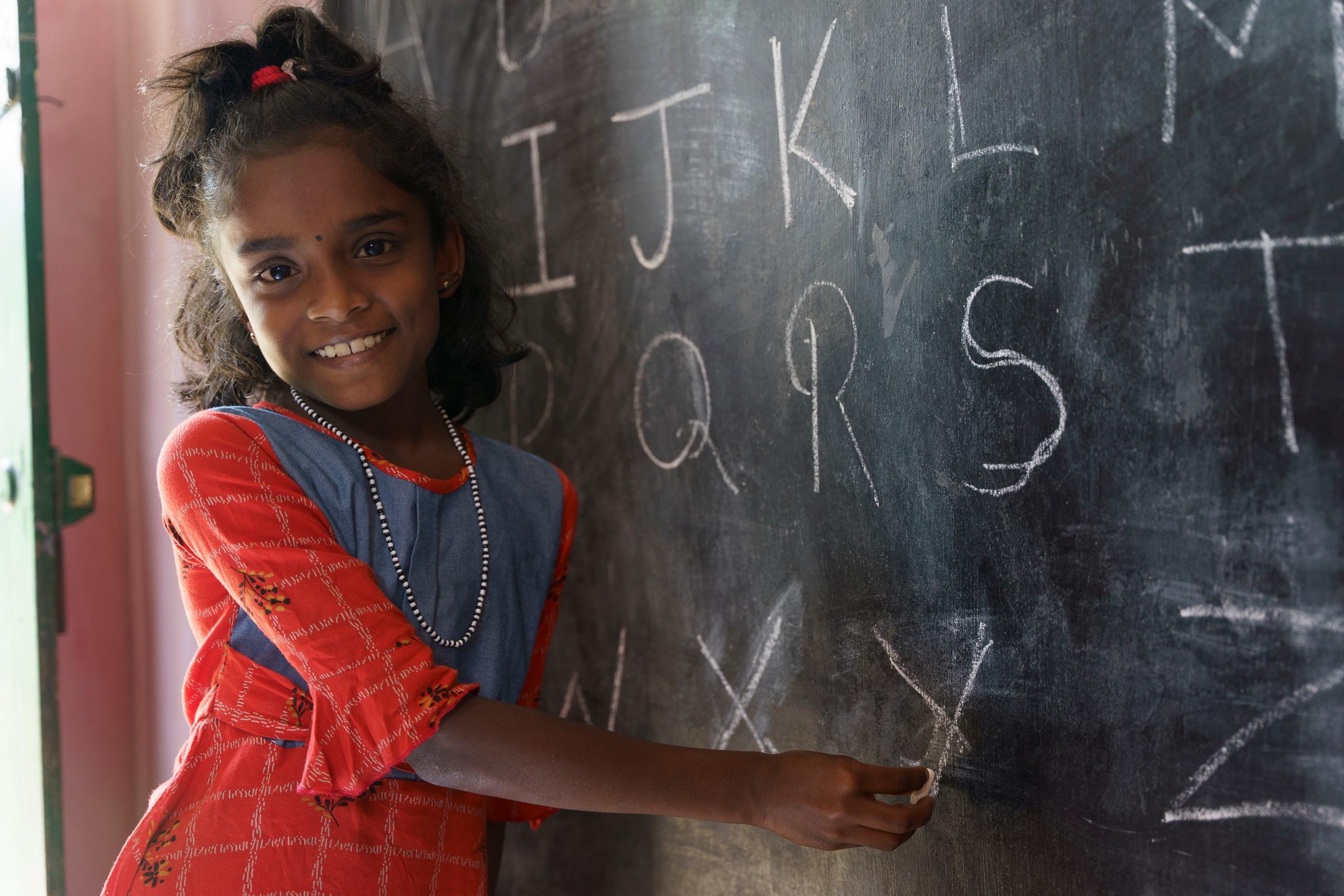 Ein Mädchen steht lachend an einer Tafel (Quelle: Christian Nusch) In den Selbsthilfegruppen lernen die Frauen auch viel über Kinderrechte (Foto: Christian Nusch)