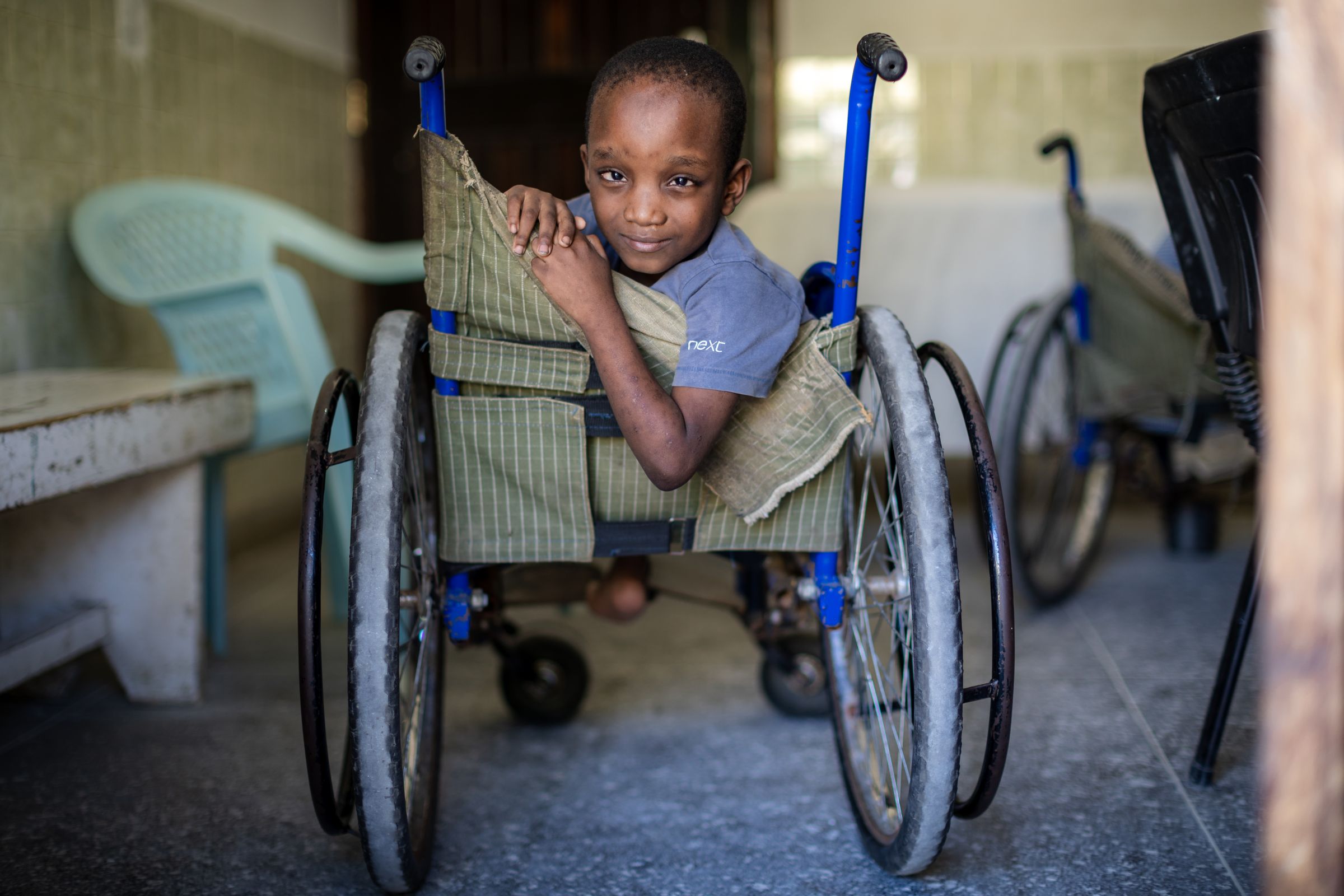 Ein kenianisches Kind sitzt im Rollstuhl. Es schaut über seine Schulte nach hinten und lächelt. (Quelle: Lars Heidrich)
